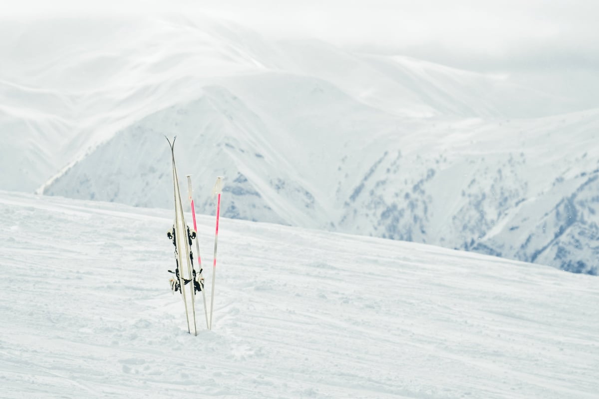 Pair of white skis with poles planted in snow on mountain slope with alpine peaks in background, concept of winter sport, ski holiday, rentals, quality gear and day off from slopes