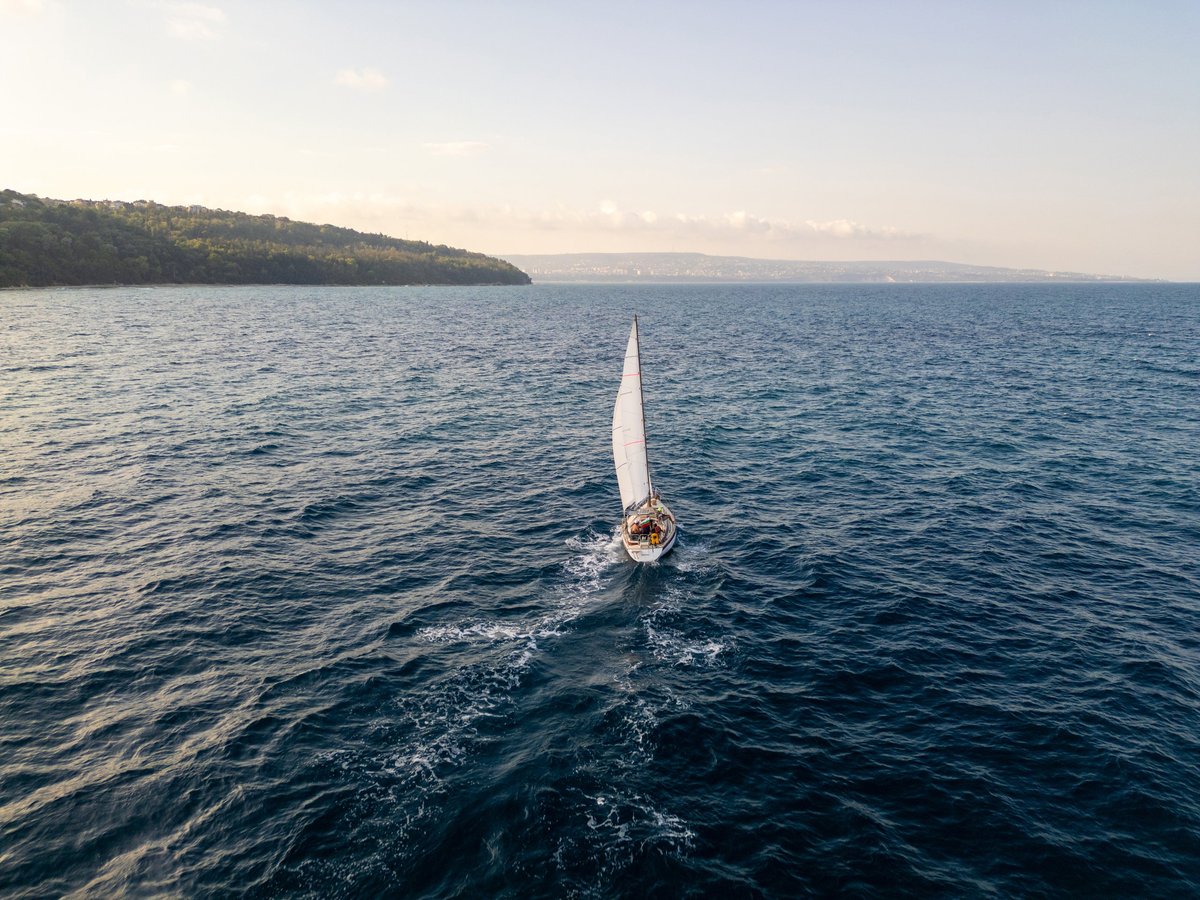 Aerial of a sailboat cruising near a scenic coastline on a calm sea at golden hour