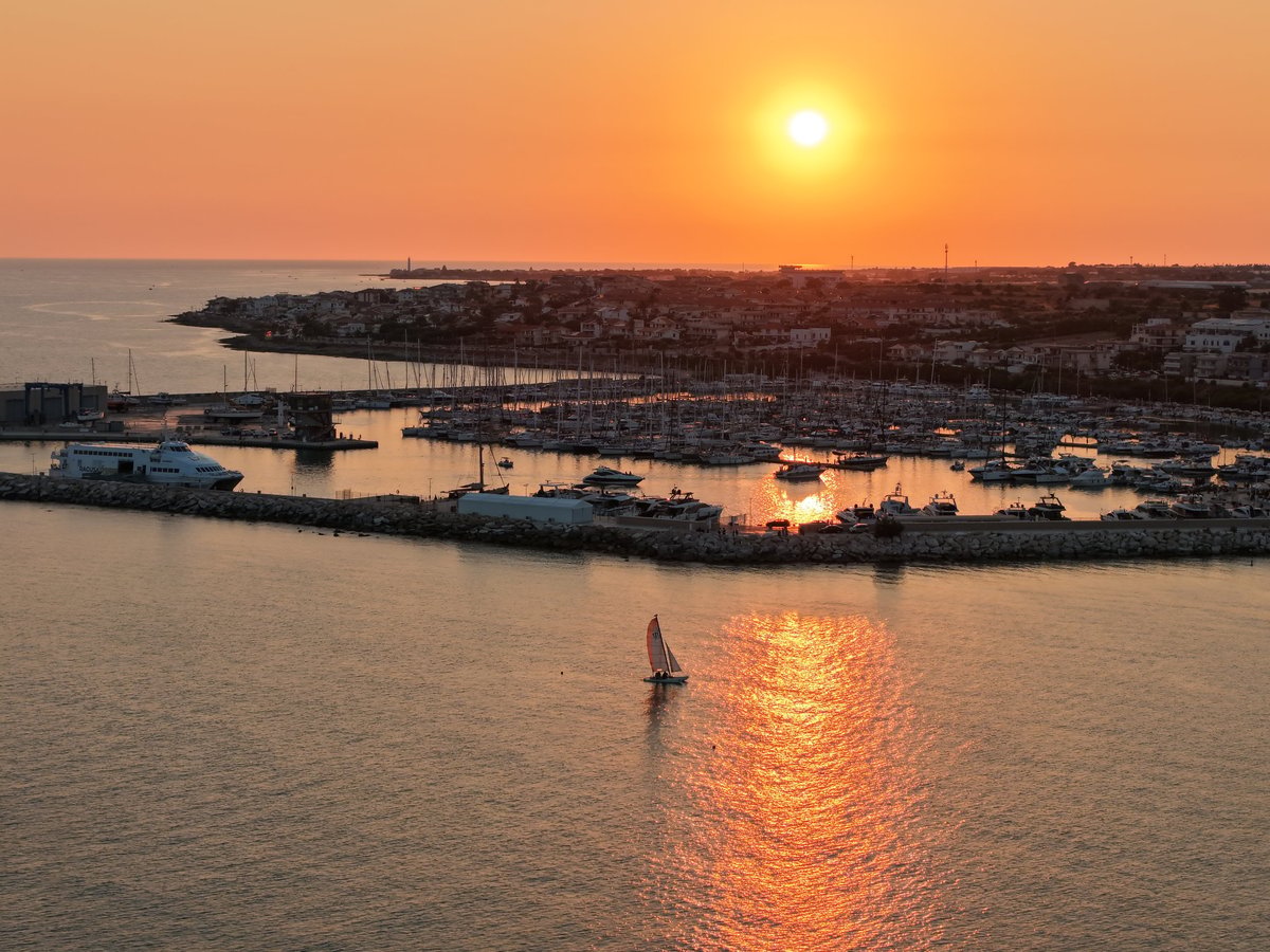 Aerial view of a serene marina at golden hour with luxury yachts moored in Mediterranean harbor