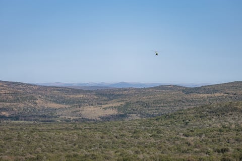 Helicopter flying above broad landscape of green and brown hills