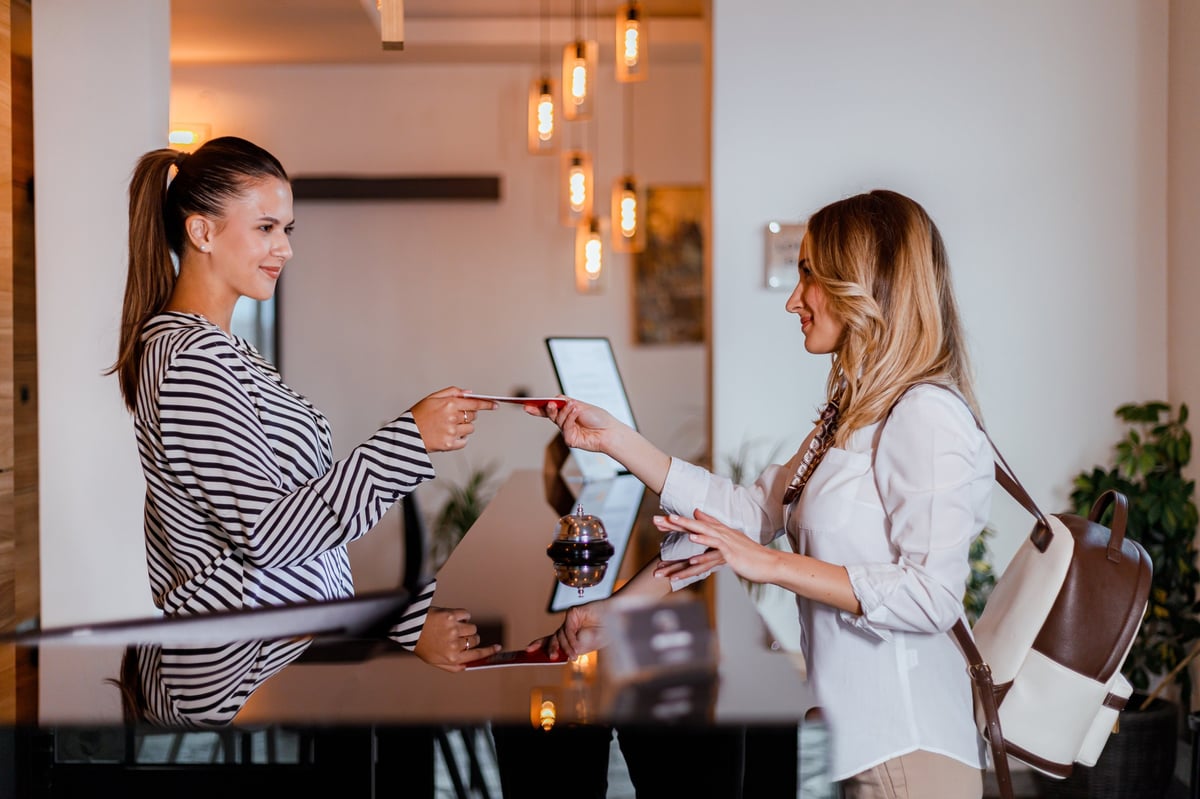 A woman interacts with a hotel receptionist while checking in. Both appear friendly and engaged in conversation.