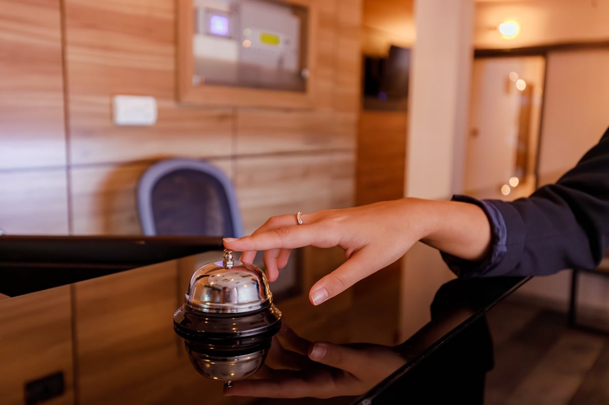 A hand touches a reception bell at a hotel signaling for assistance