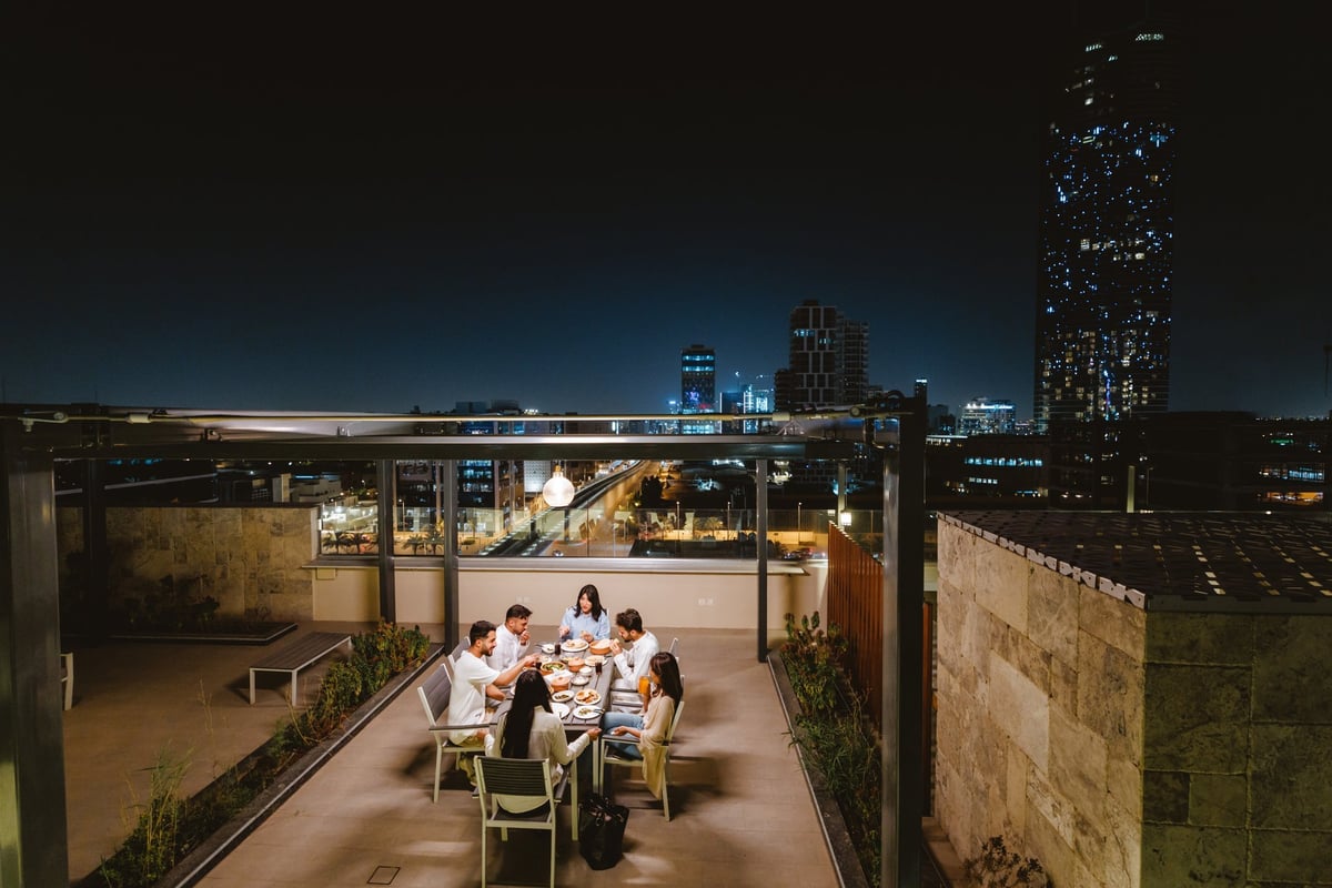 Friends enjoying a lively dinner on a rooftop terrace with cityscape at night