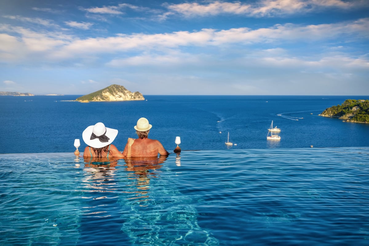 A romantic holiday couple in a swimming pool watches the summer sunset over the mediterranean sea