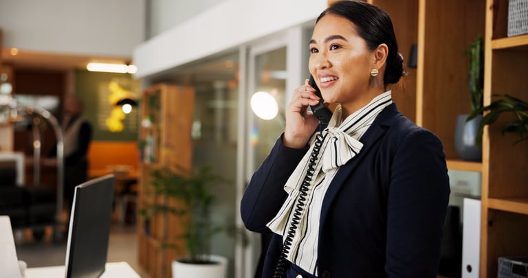 Woman, phone call and happy at hotel, concierge and talk with client for booking information. Person, help desk and receptionist with telephone, contact and listen with hospitality service at lodge