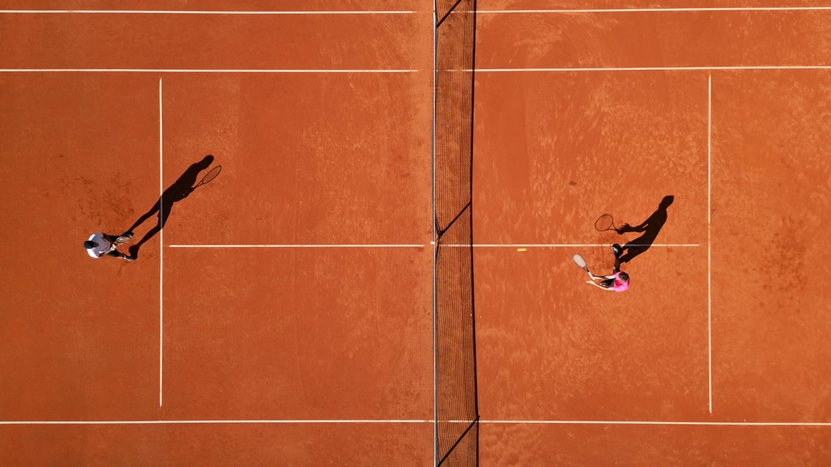 Two athletes practice tennis on a vibrant clay court, showcasing focused training and skill development, captured with an aerial shot