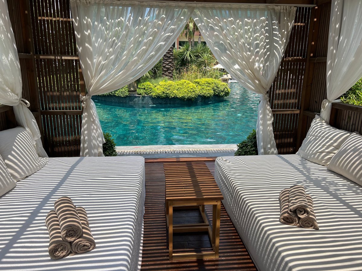 Wooden lounger with white curtains and pool view
