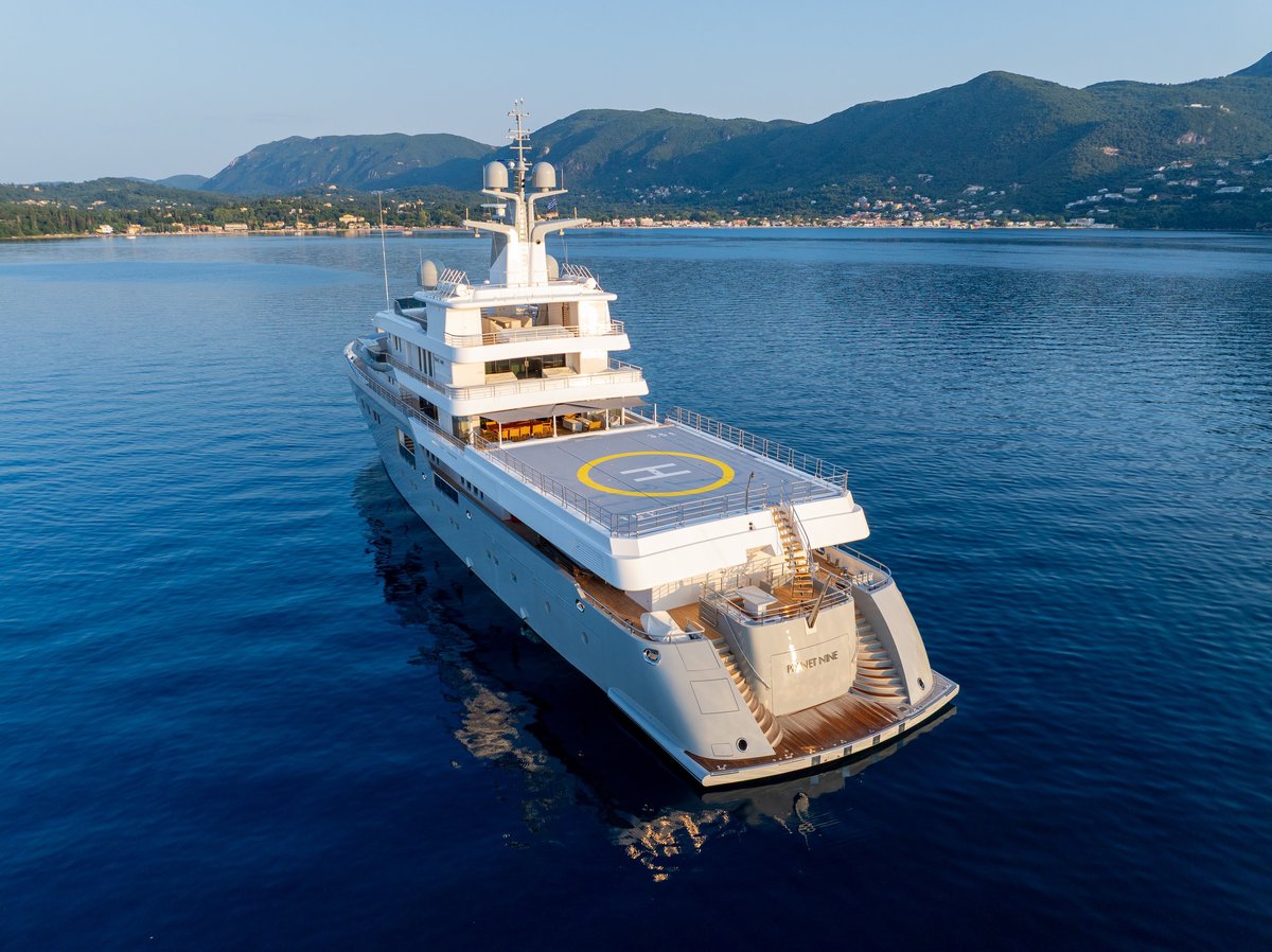 Aerial drone view of a luxury superyacht with a helipad, anchored in a calm turquoise bay
