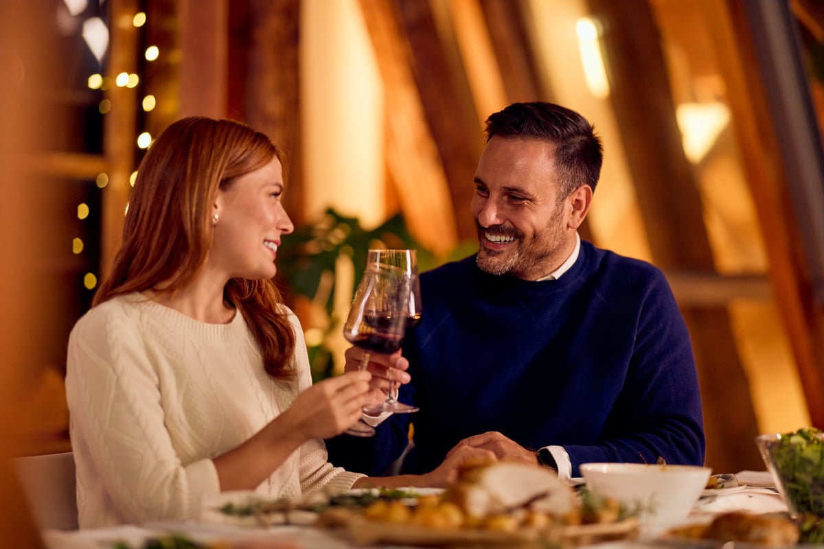 Two adults enjoy a cheerful toast over a meal, wine, and cozy lighting