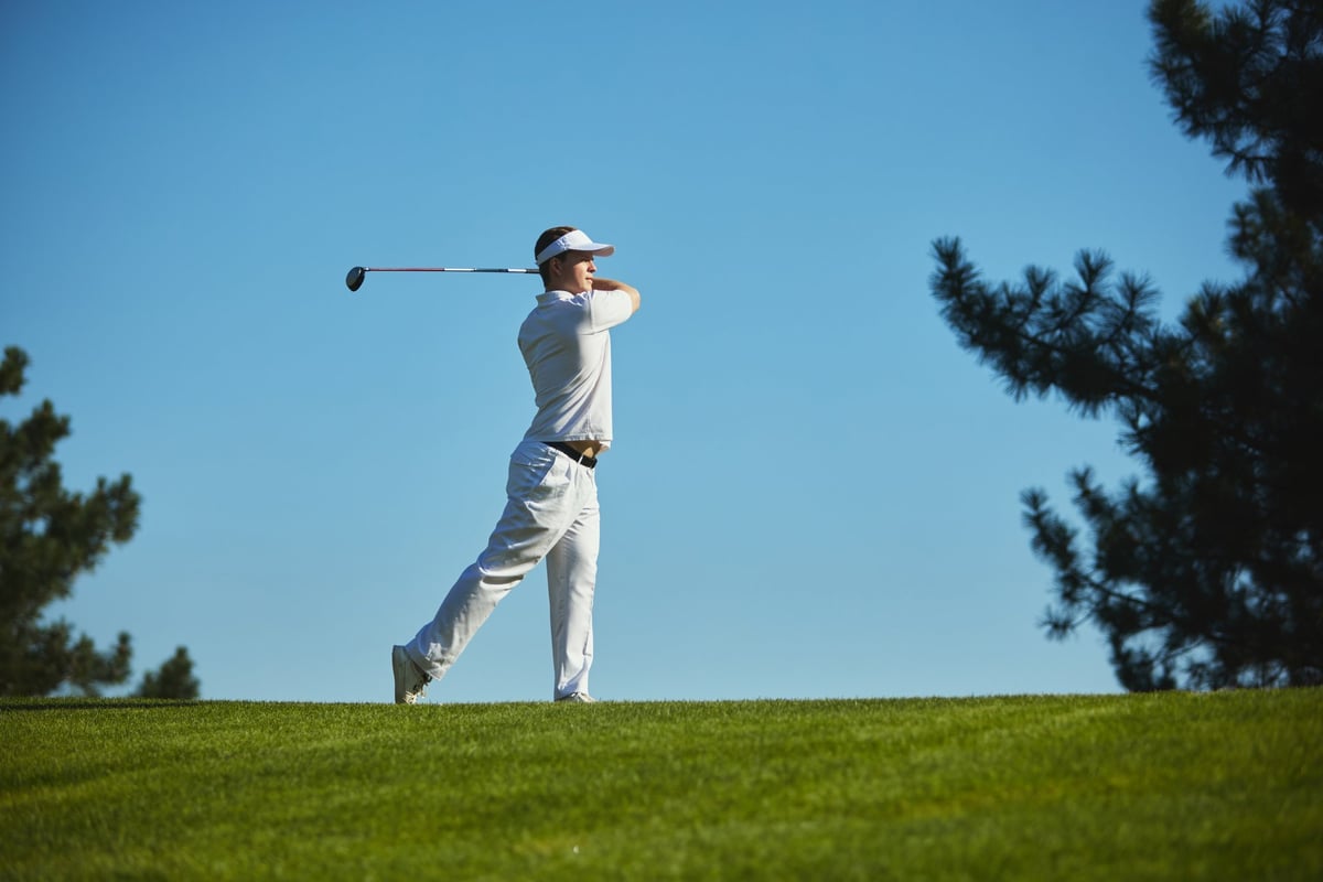 Golfer completing dynamic swing on sunny golf course
