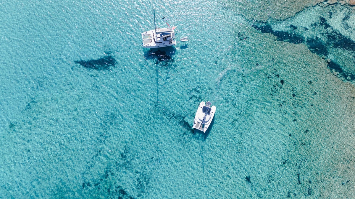 Top-down aerial view of catamarans anchored in crystal clear turquoise water