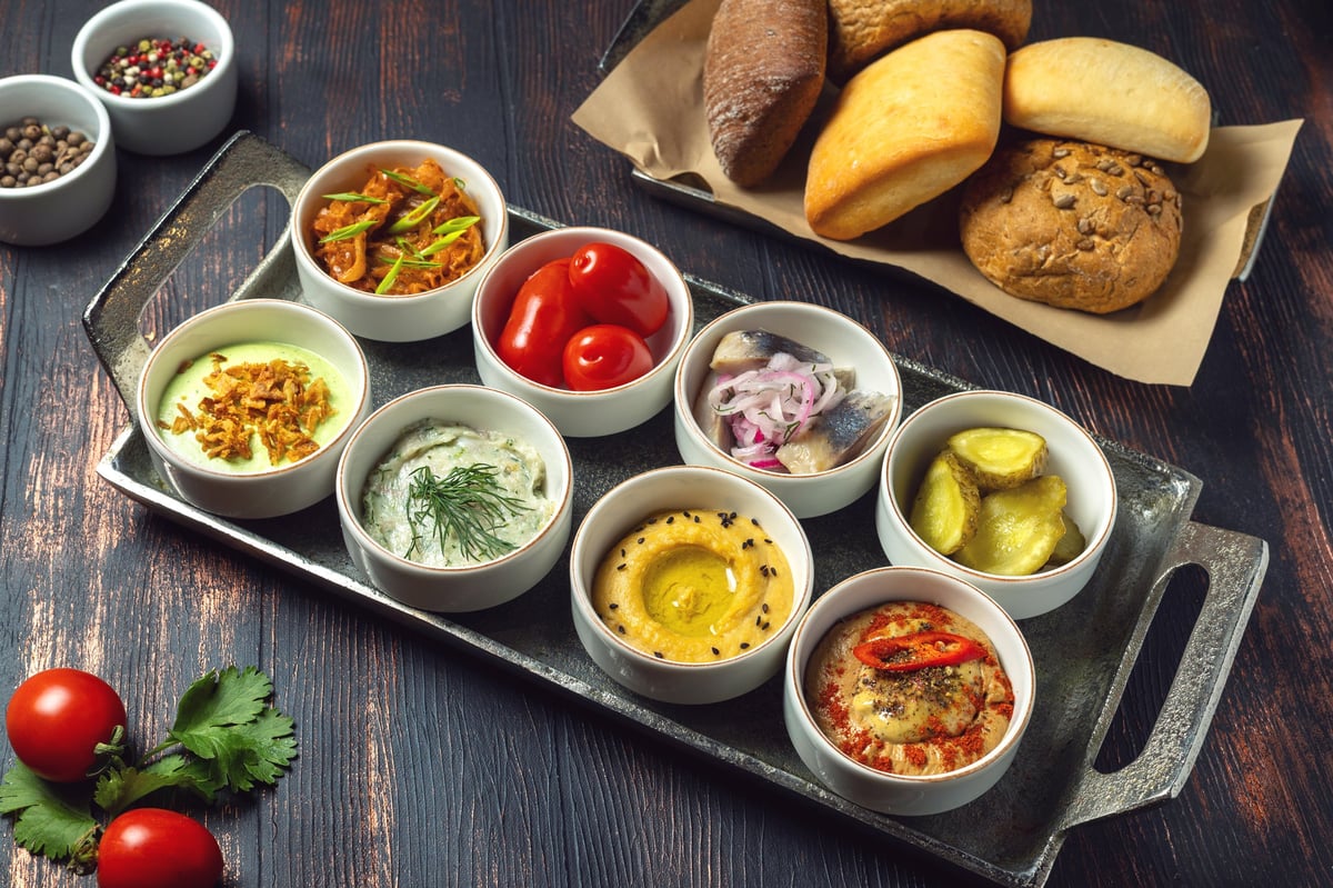 Assorted appetizers in small white bowls on metal tray variety of dips meze sharing platter
