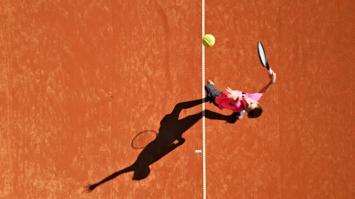 Player in vibrant pink shirt practices on a clay court mid-action