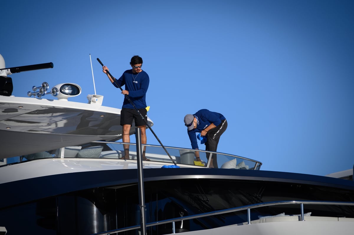 Two crew members on a sleek luxury yacht with polished railings and blue skies