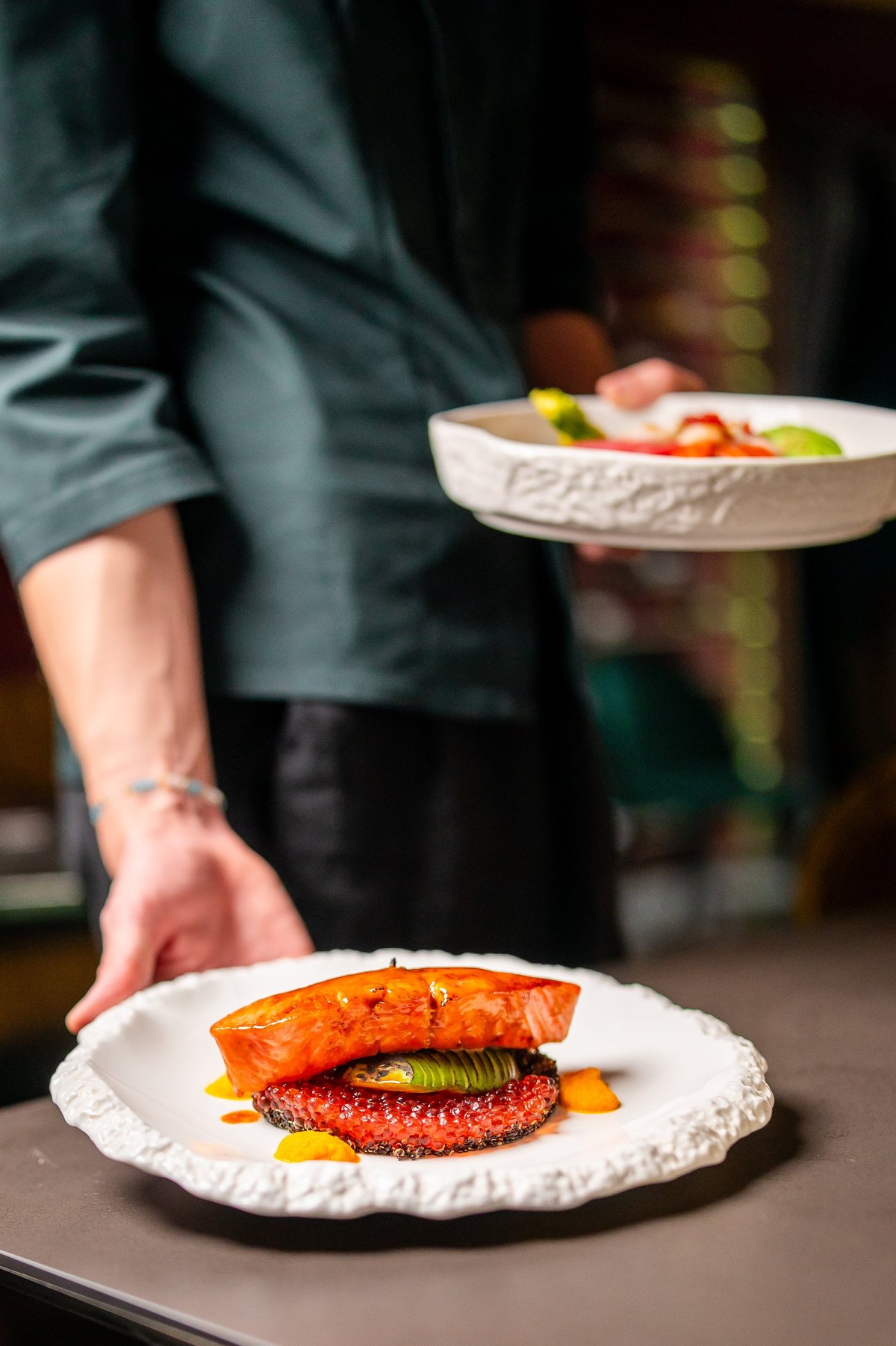 A professional chef plates a delicious seared salmon dish with a green vegetable and orange garnish