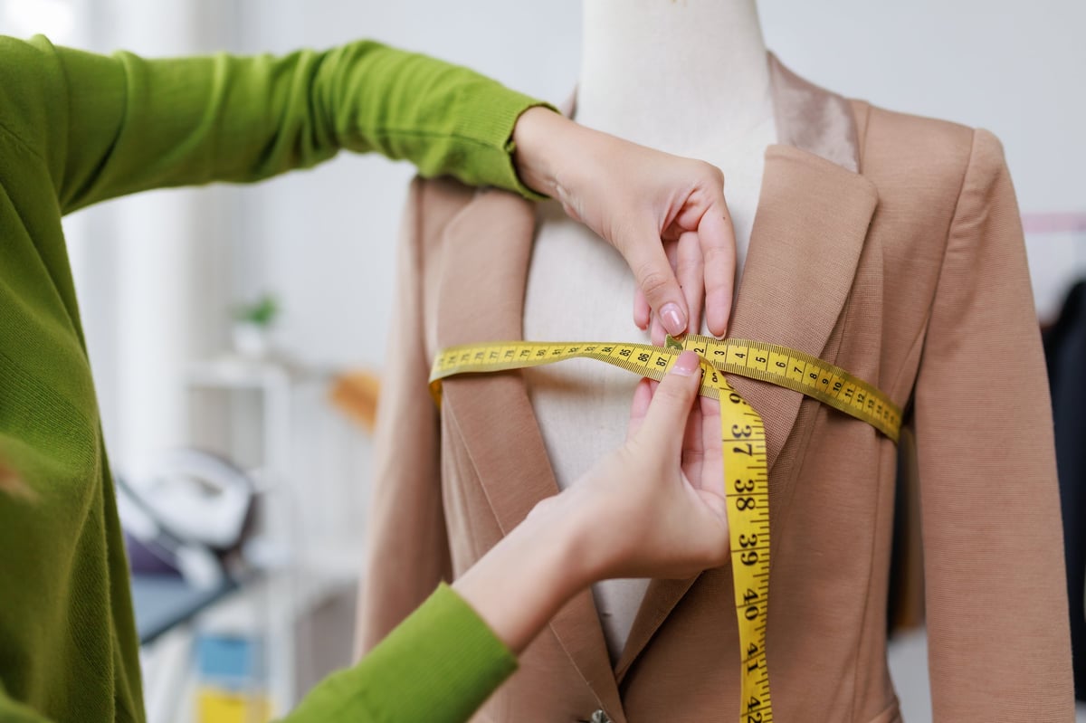 Seamstress is working in her atelier, carefully measuring the chest area of a tailored jacket draped on a mannequin, ensuring a perfect fit for the client
