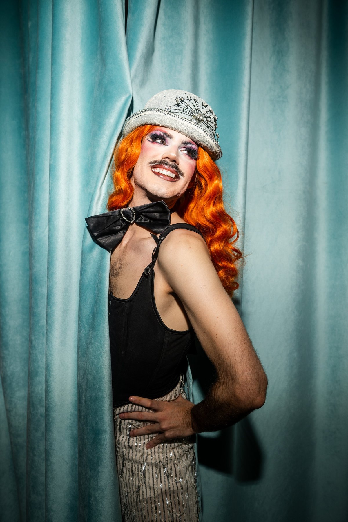 Drag performer smiling in front of stage curtains at a lively cabaret