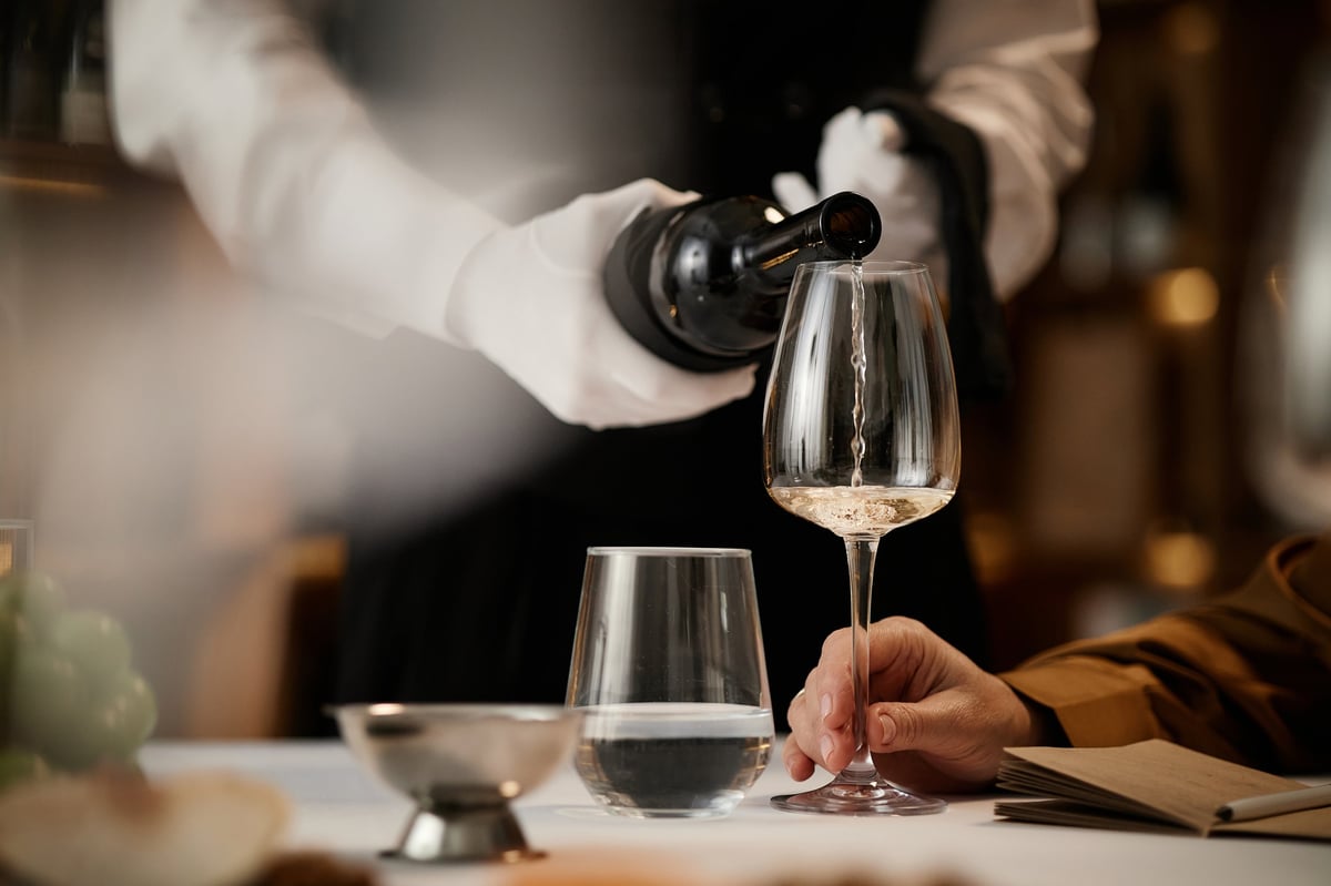 Sommelier pouring white wine during tasting session at fine dining table, closeup of hands and glassware