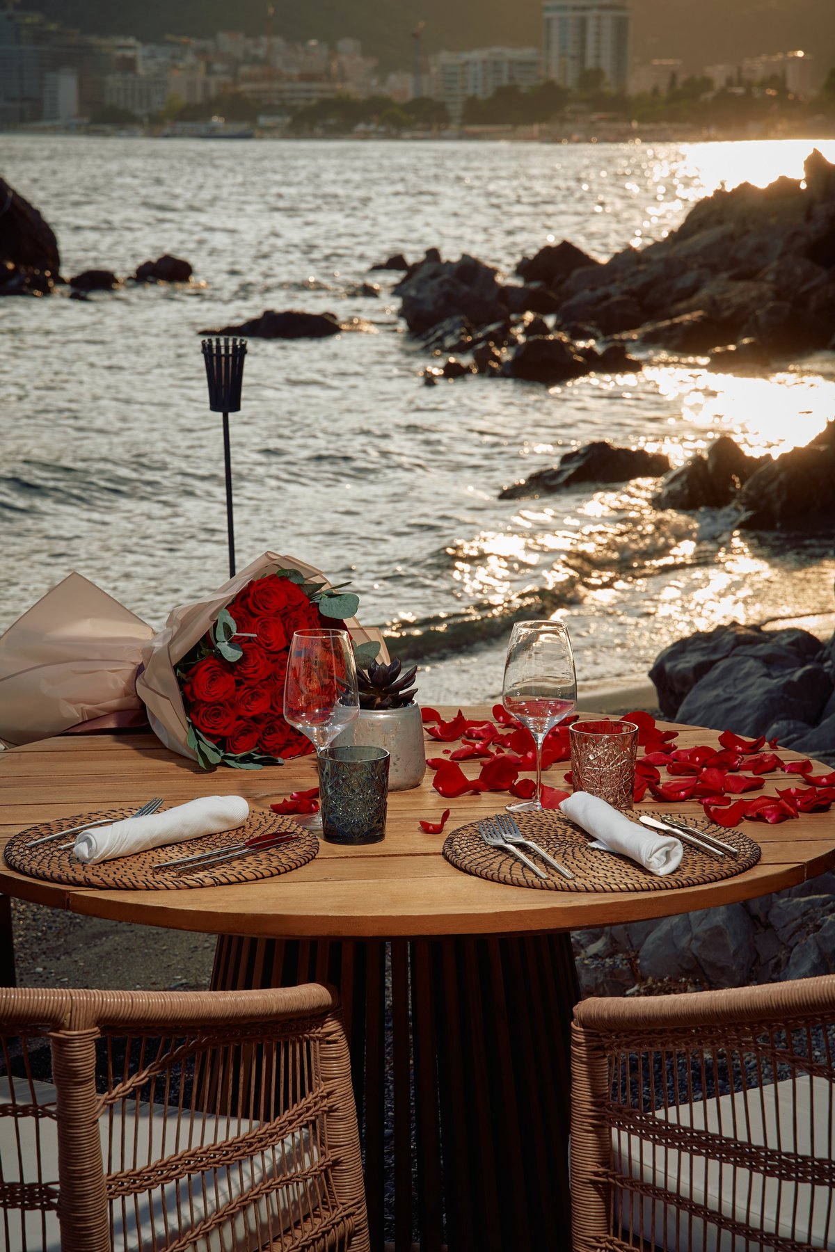 Romantic beachside dinner setup with roses, elegant tableware, and scenic ocean view at sunset for an unforgettable evening experience