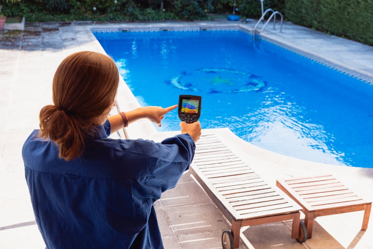 Woman using a thermal imaging camera to check the temperature of a backyard swimming pool
