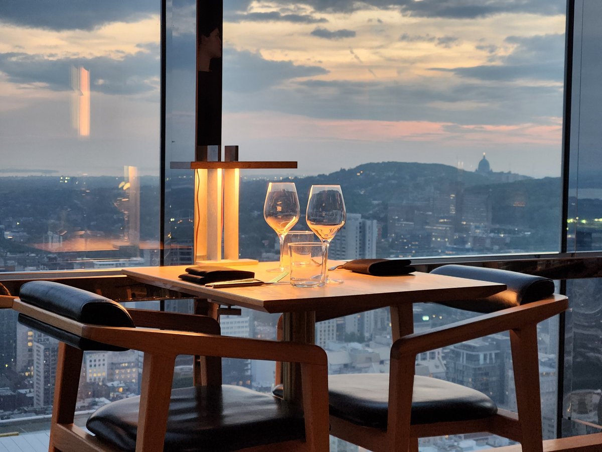 Elegant restaurant table set with wine glasses and soft ambient lighting overlooking a city skyline at sunset