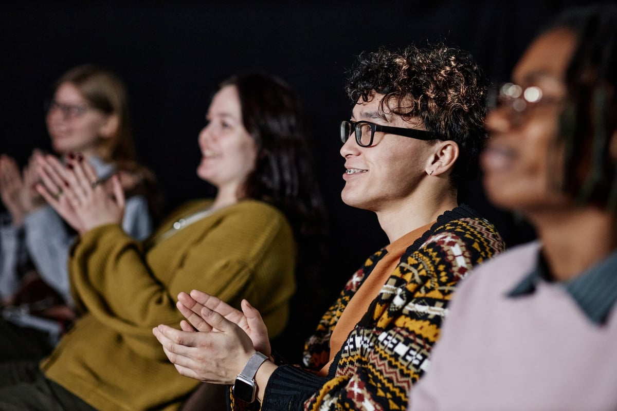 Group of diverse adults sitting in row clapping and smiling at an indoor event