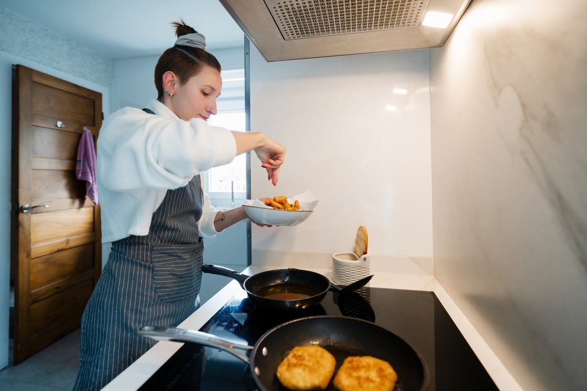 Person seasoning freshly fried food in a pan in a contemporary kitchen