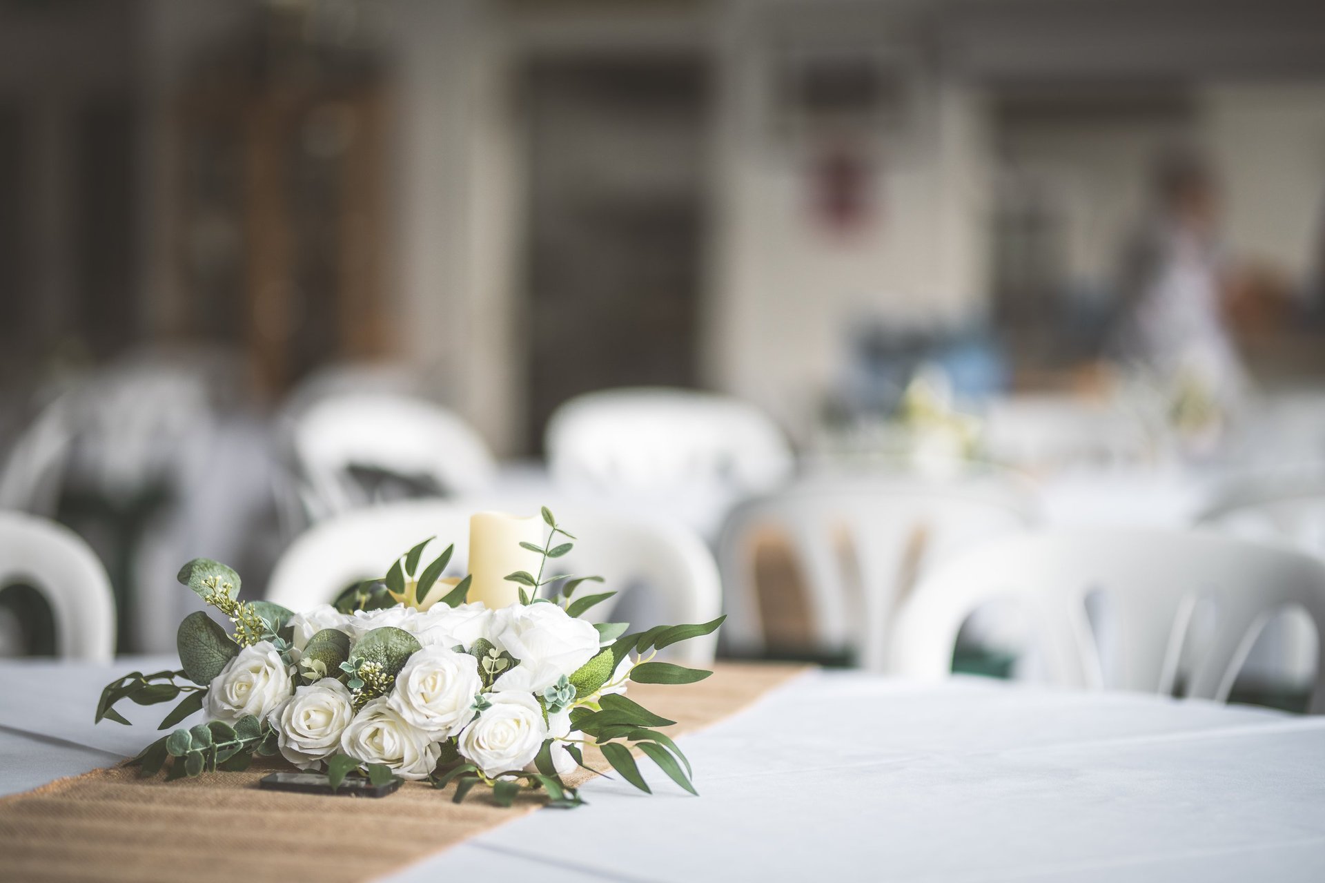 A beautiful floral arrangement and candle sit on a table set for a wedding reception, creating a romantic atmosphere