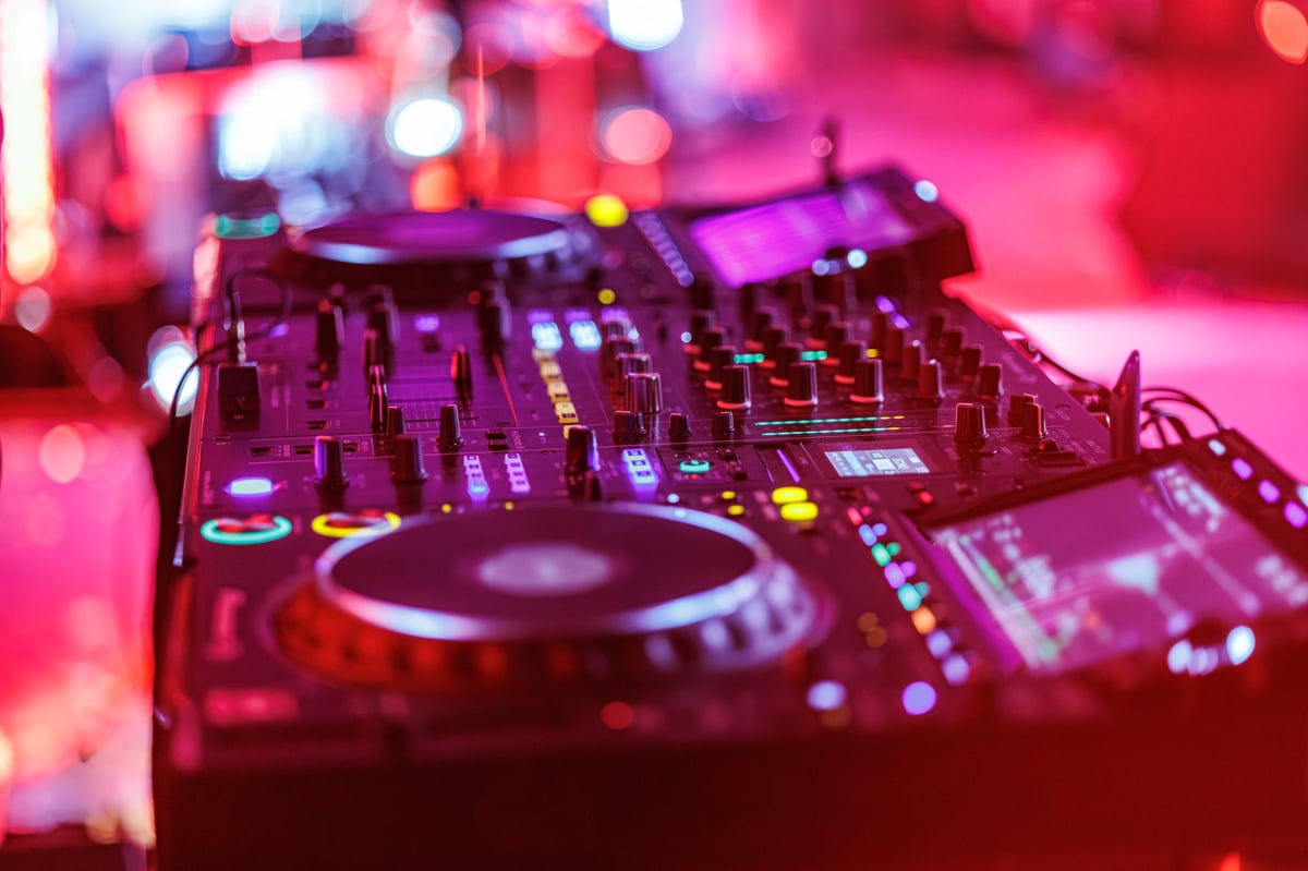 DJ performing on professional mixer with vibrant nightclub lighting and crowd atmosphere