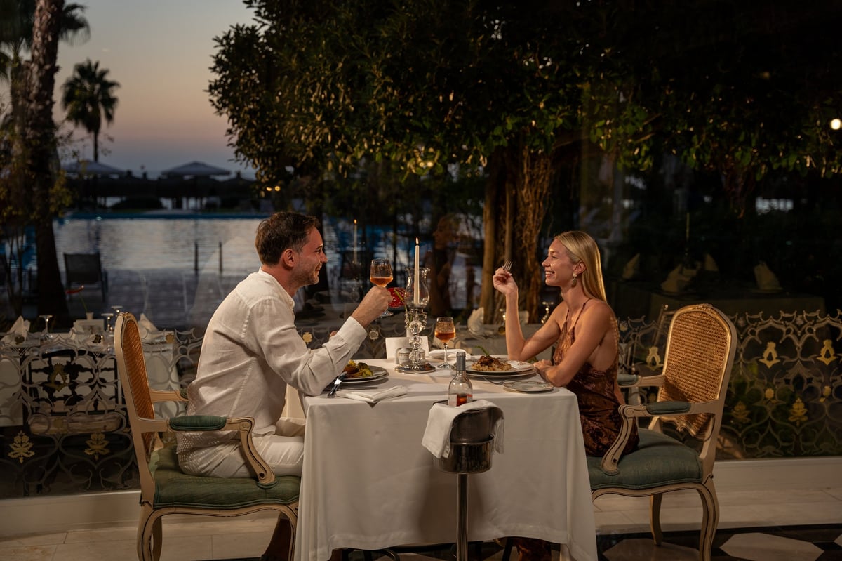 Romantic couple toasting with wine glasses at sunset outdoor dinner