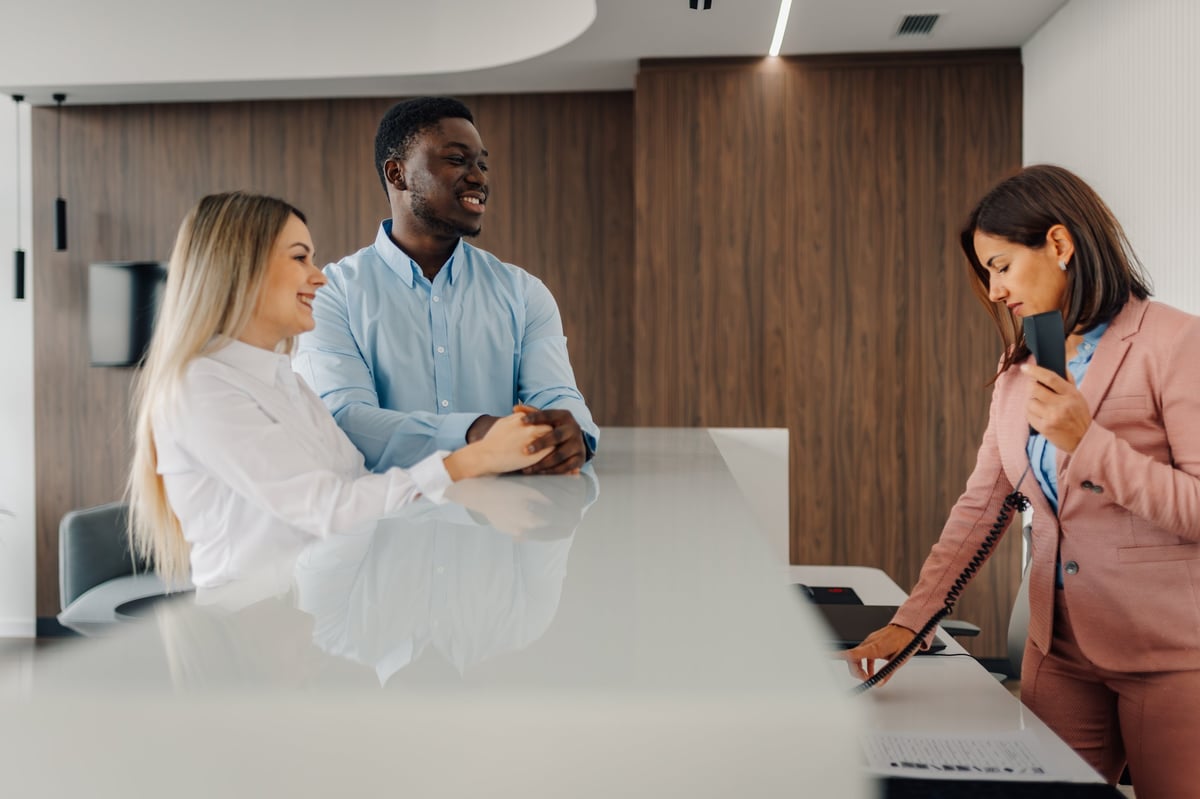 Diverse couple smiling, checking in at a modern hotel reception desk, receiving excellent service