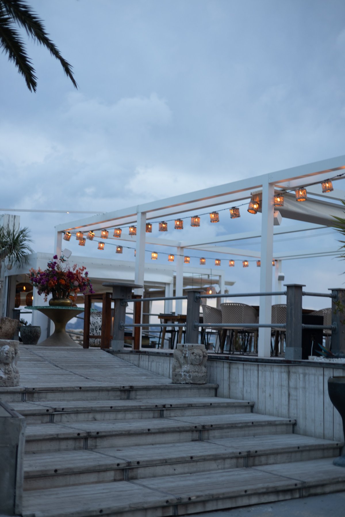 Charming terrace with string lights, elegant floral arrangement, and scenic sky backdrop for evening dining or events