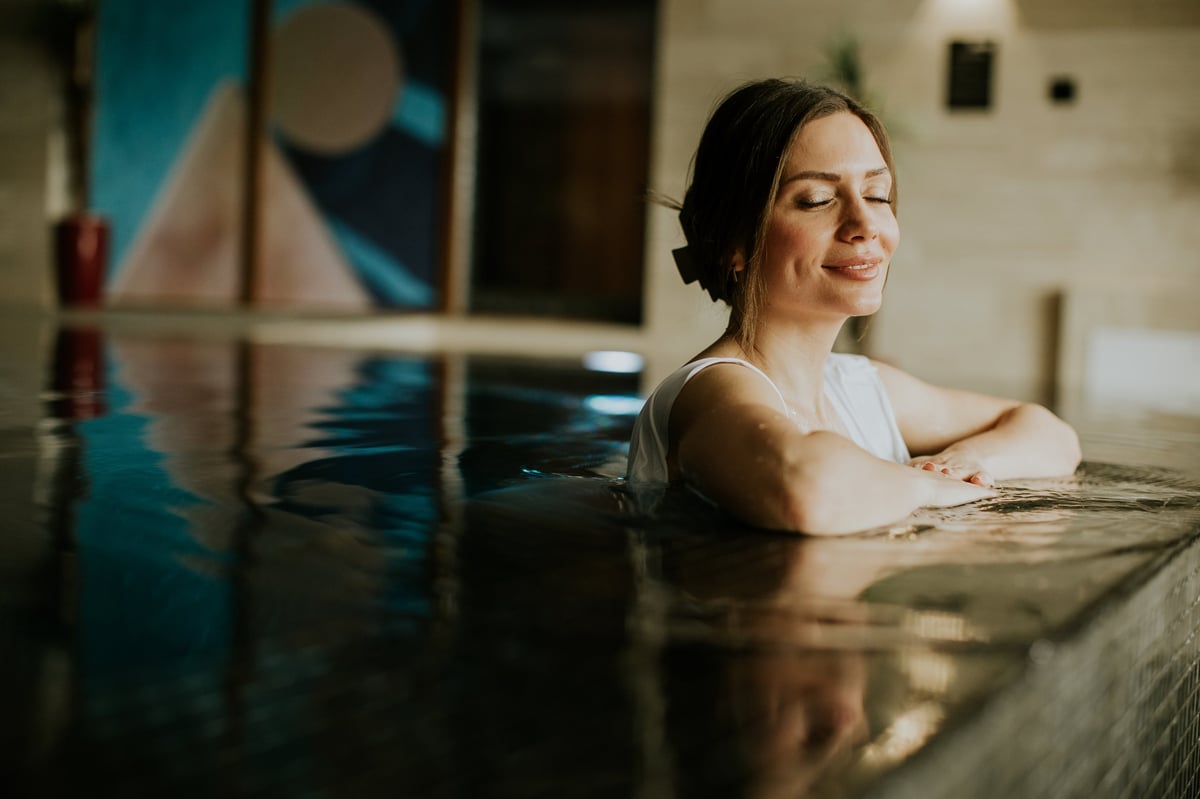 A woman enjoys time in a water area at a spa. She looks relaxed with her eyes closed.