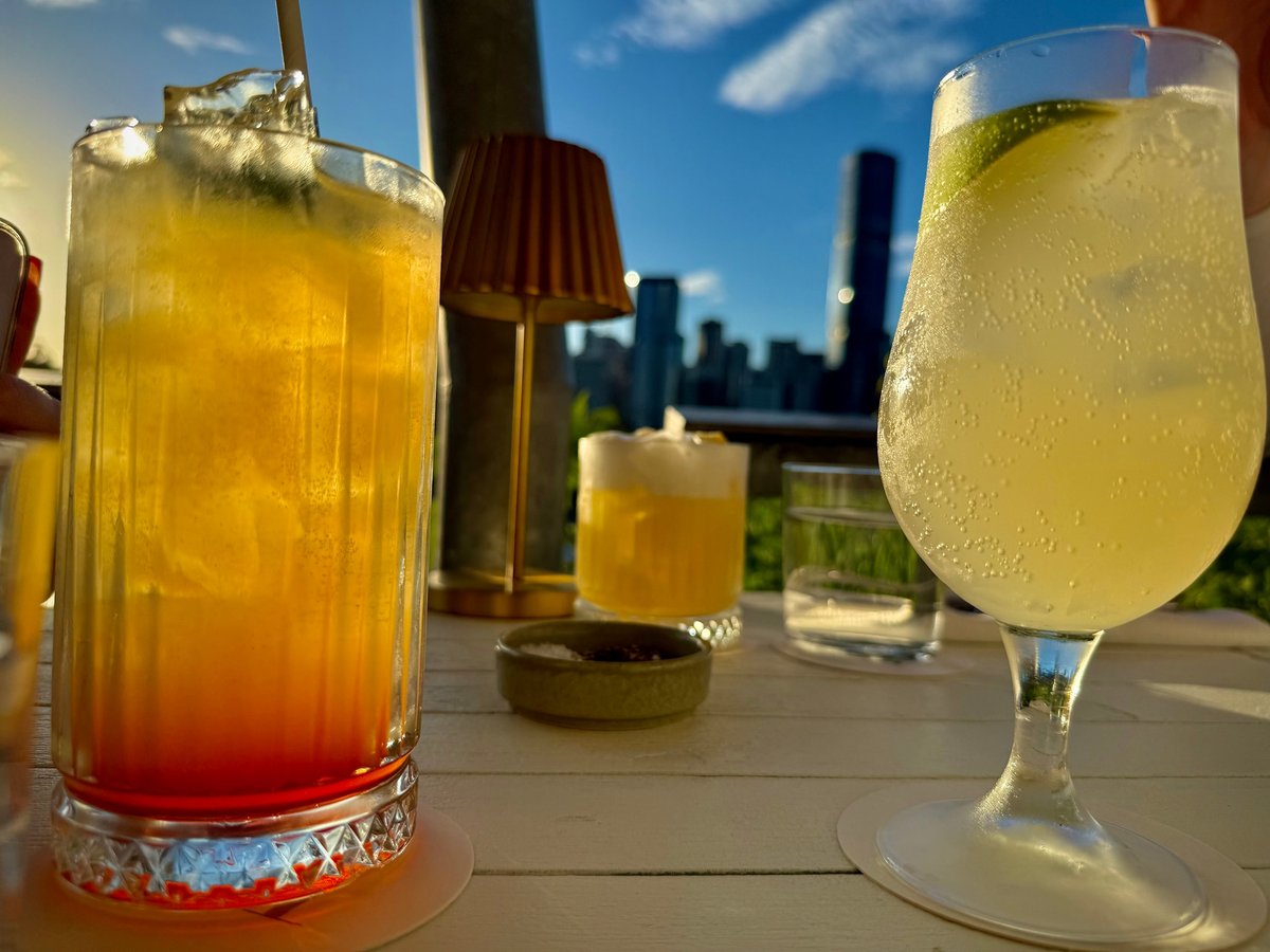 Refreshing cocktails served on an outdoor rooftop bar at sunset with the city skyline in the background, warm evening light