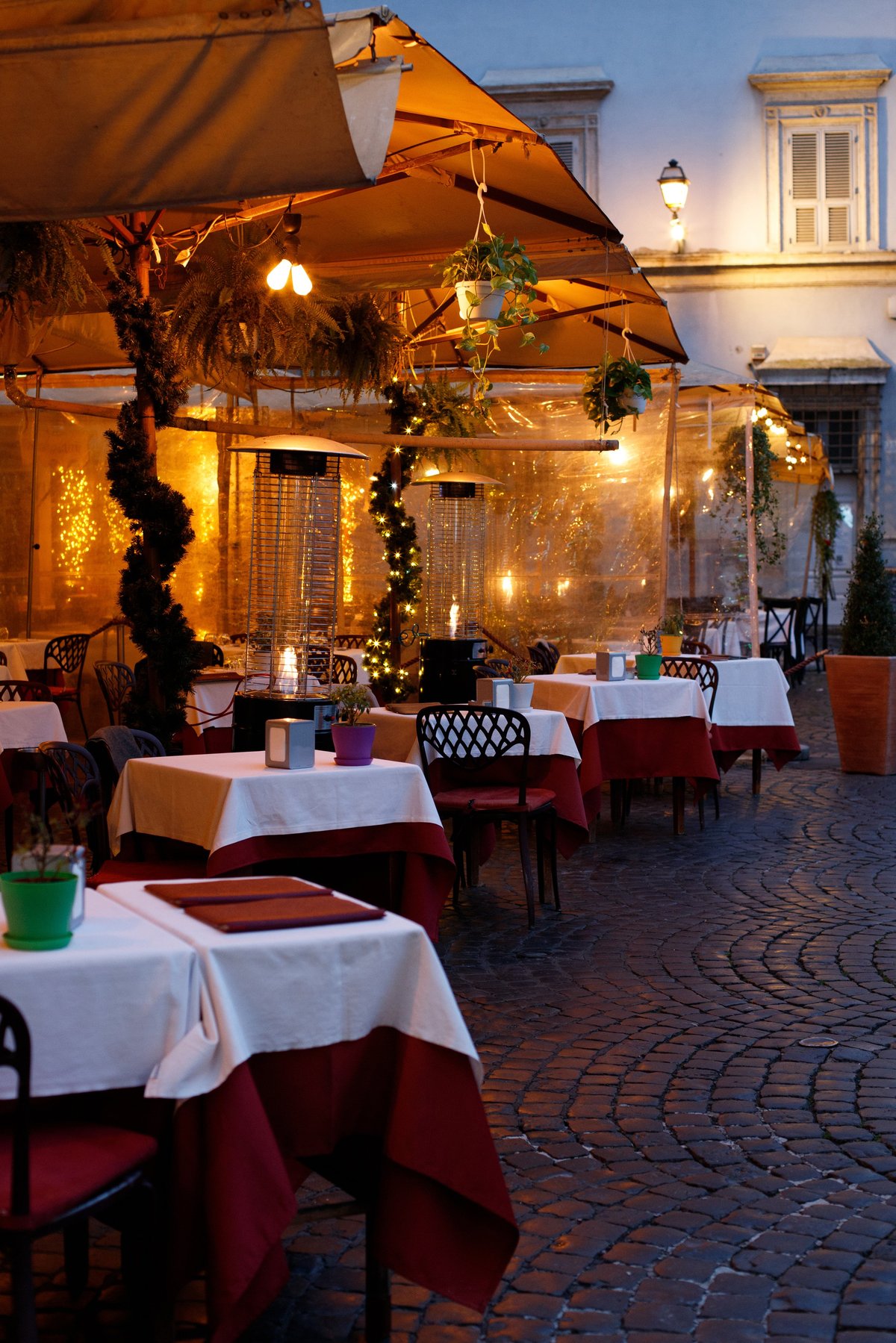 Cozy outdoor restaurant terrace at night with warm lighting and decorated tables on a cobblestone street in Rome