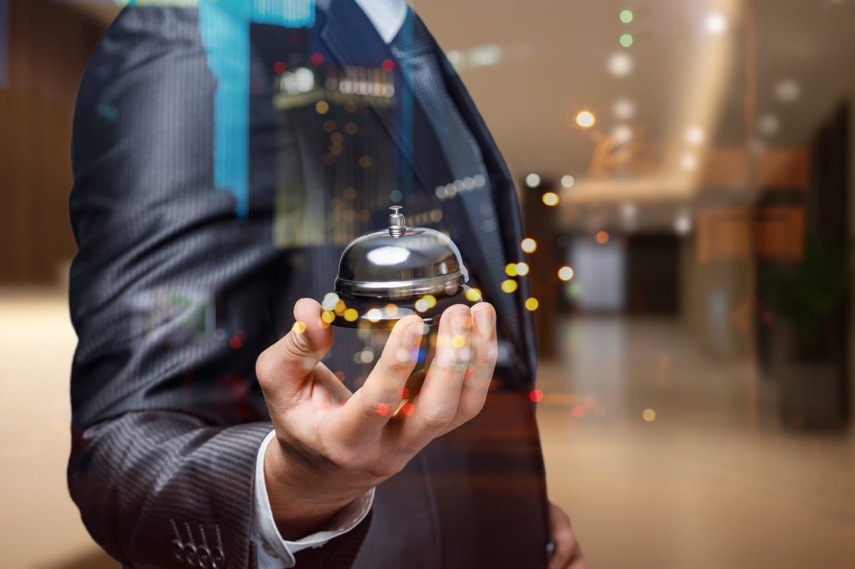 A well-dressed man holds a silver service bell in a luxurious hotel lobby
