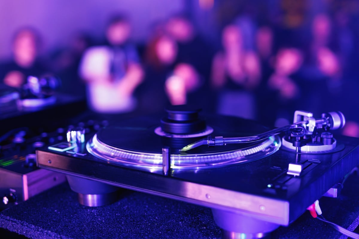 A close-up of a record player spinning a disc with ambient lighting and a blurred crowd