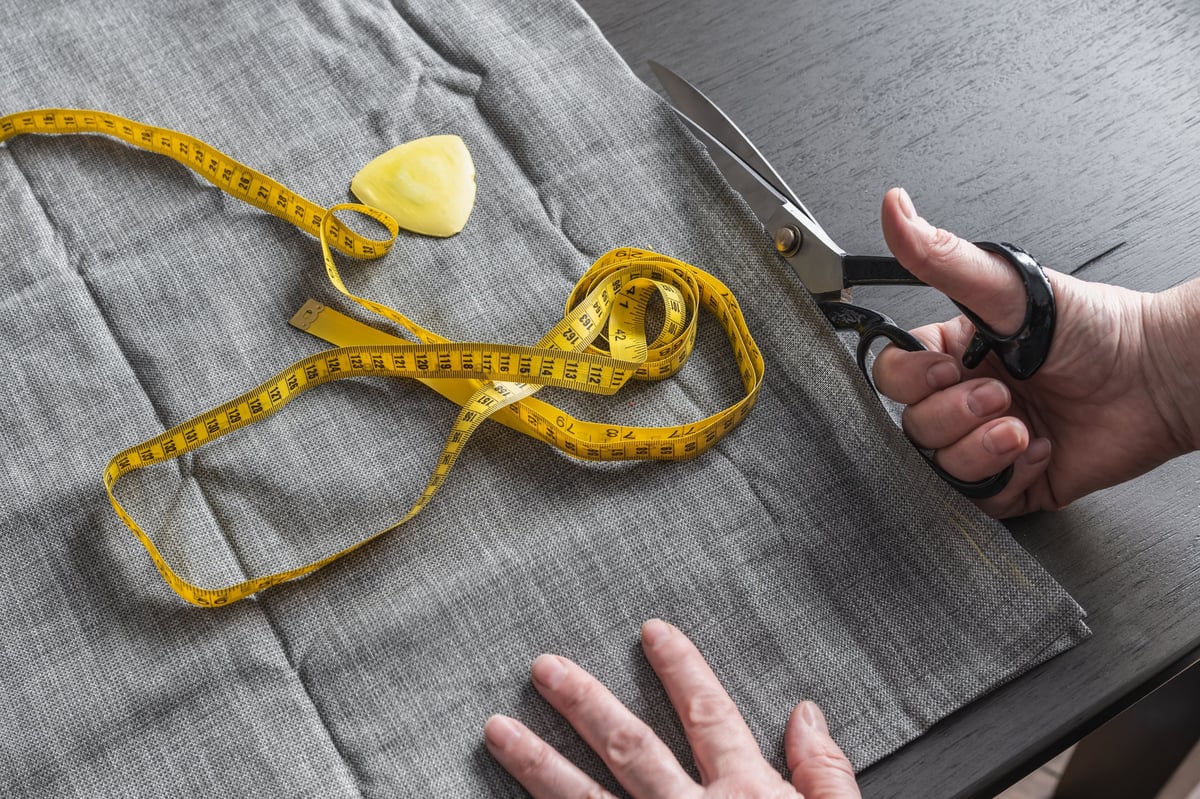 Hand cutting fabric with scissors. Yellow tape measure and tailor's chalk. Careful preparation and technique required for working with fabric.