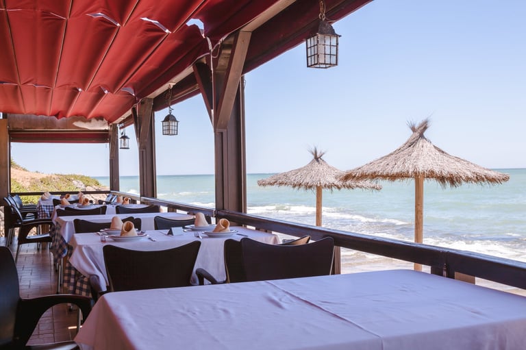 A covered outdoor beach restaurant overlooking the ocean on a bright sunny day