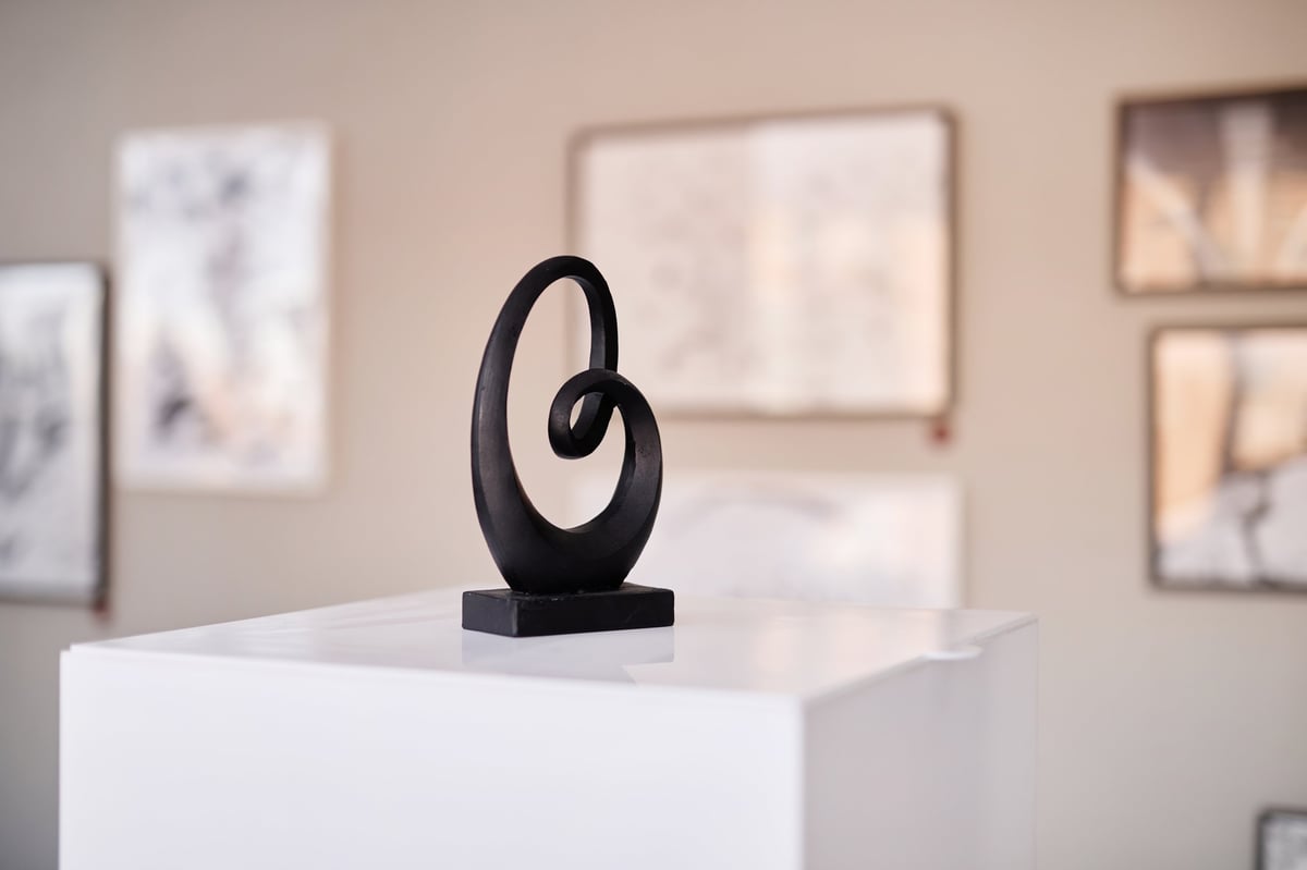Abstract black sculpture standing on pedestal in contemporary art gallery