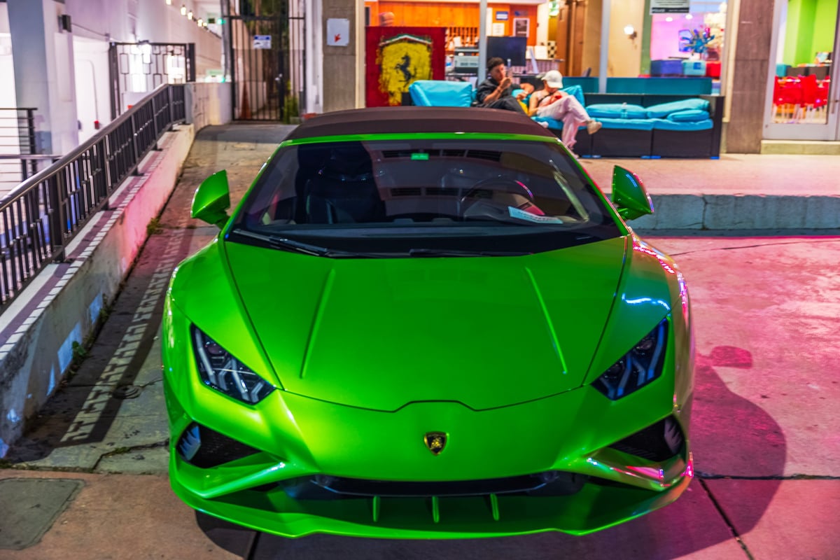 Miami Beach. USA. Close up front view of bright green Lamborghini Huracan sports car shining under colorful evening city lights.