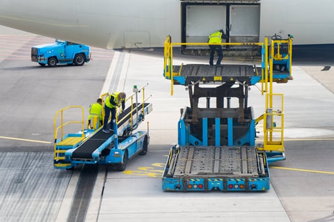 Airside cargo equipment and airport workers under a jet, highlighting ground support operations