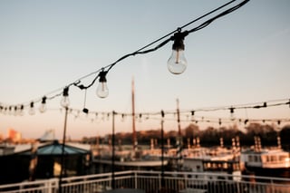 String lights glow over a marina at golden hour framing an urban skyline