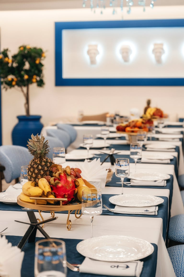 Long Banquet Table With Fruit Centerpieces, Pineapple And Grapes On Platters, Layered White Plates, .