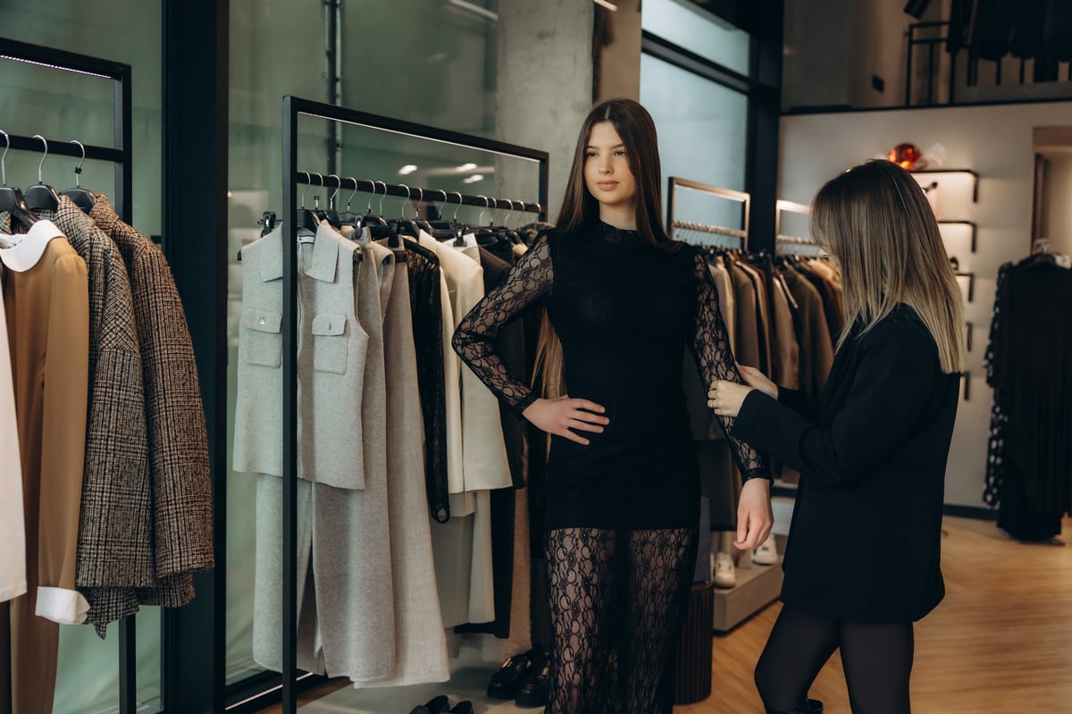 Personal stylist assisting female client during fitting session for black lace dress in modern boutique