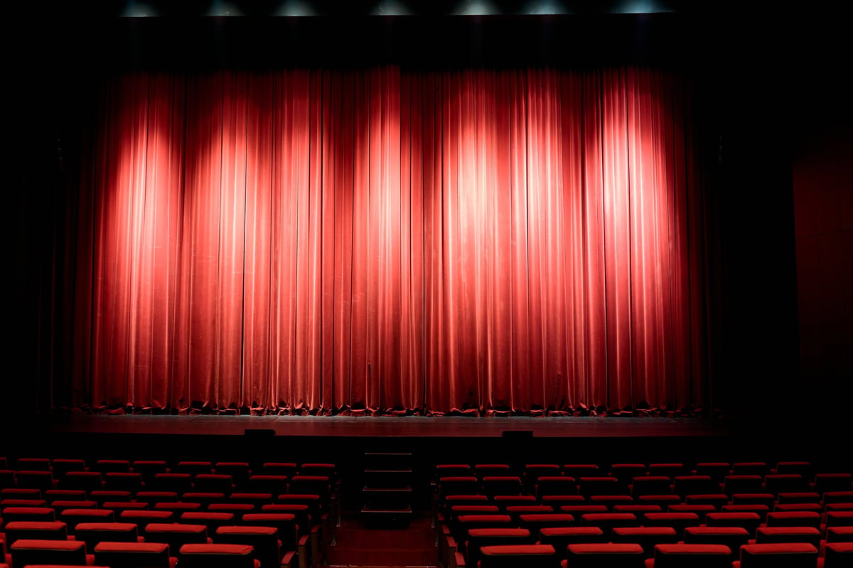 Empty theater stage with a dramatic red velvet curtain illuminated by spotlights, awaiting a performance in the dark auditorium