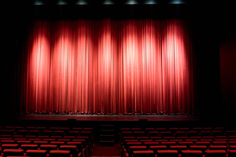 Empty theater stage with a dramatic red velvet curtain illuminated by spotlights