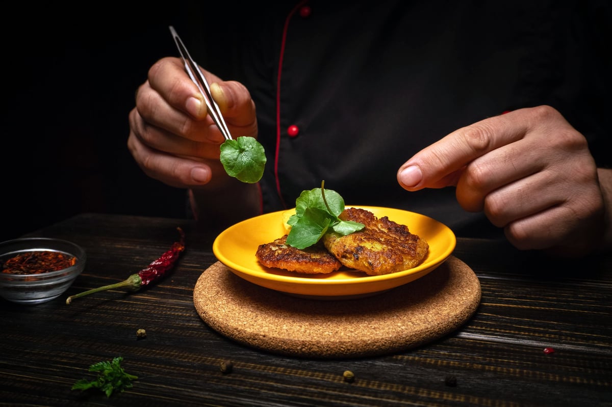 A chef is arranging food on a plate using tweezers in a dimly lit setting