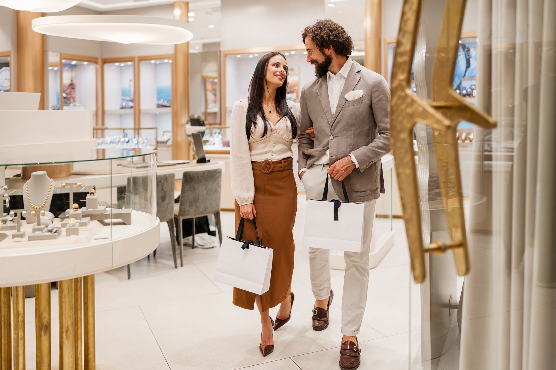 Well-dressed man and woman carrying shopping bags walking through luxury jewelry boutique