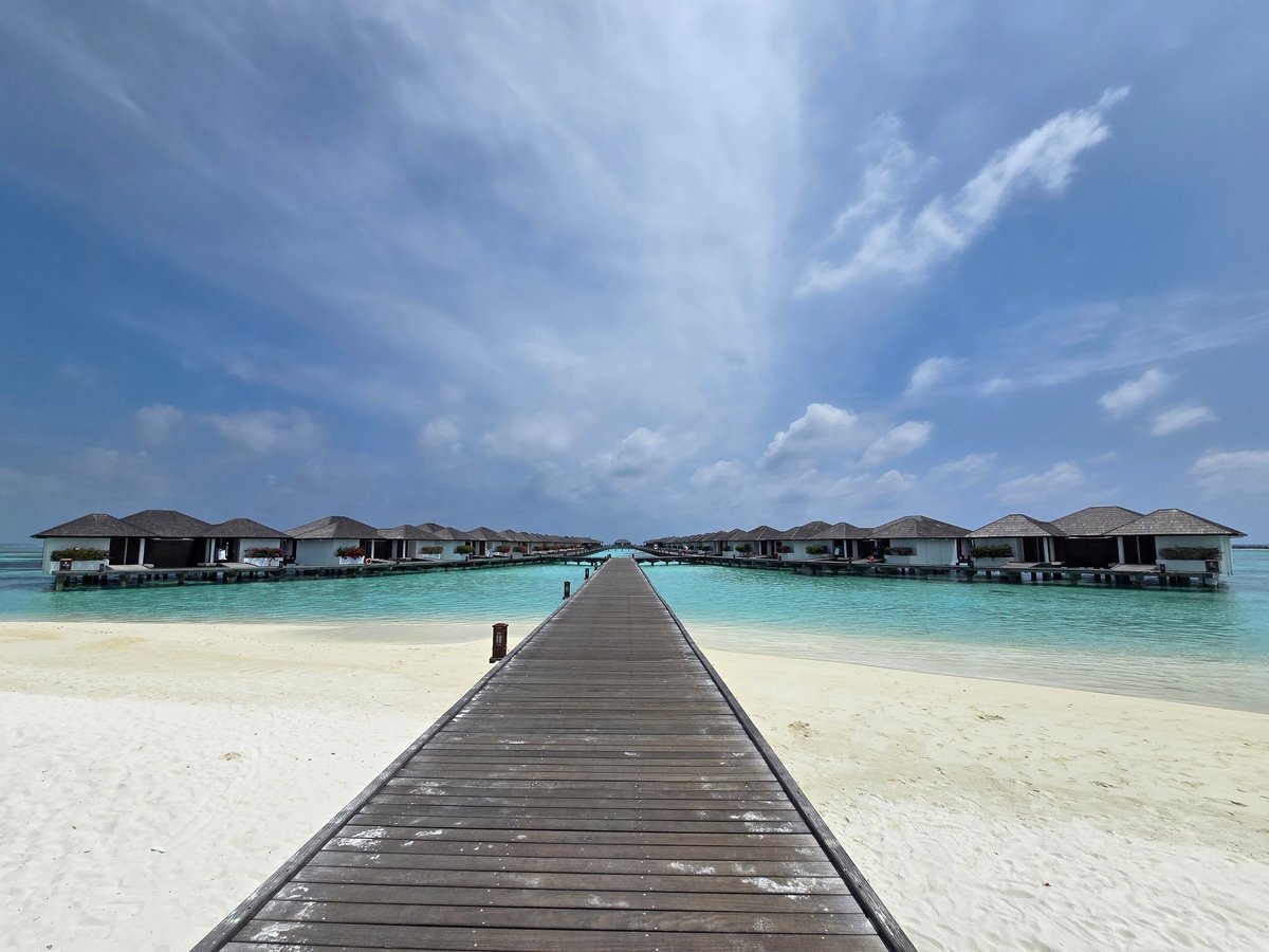 A walkway leads to overwater villas in Maldives with blue lagoon and white sand beach